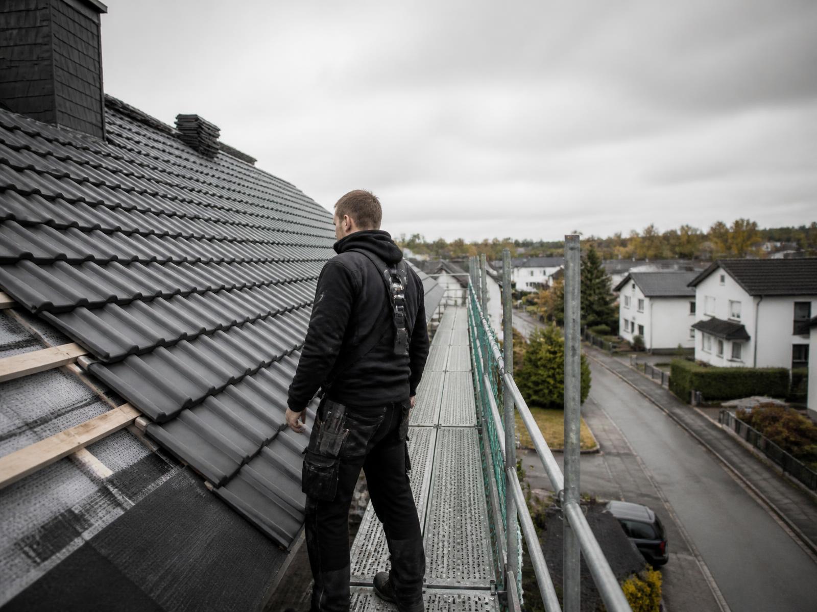 Gesicherter Handwerker auf dem Gerüst am Dachrand eines Wohnhauses